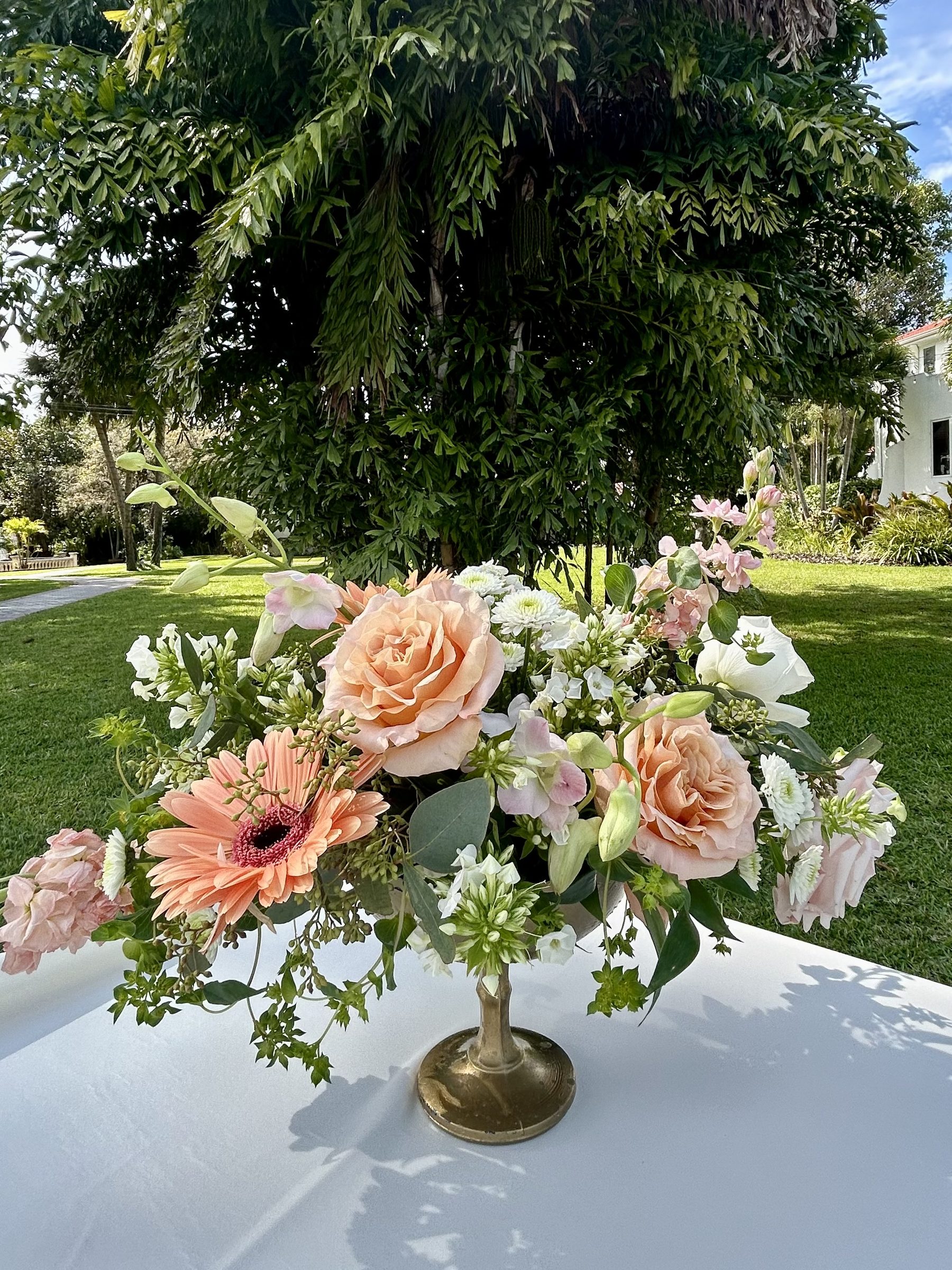Coral and peach garden bouquet on a brass pedestal in a sunlit garden