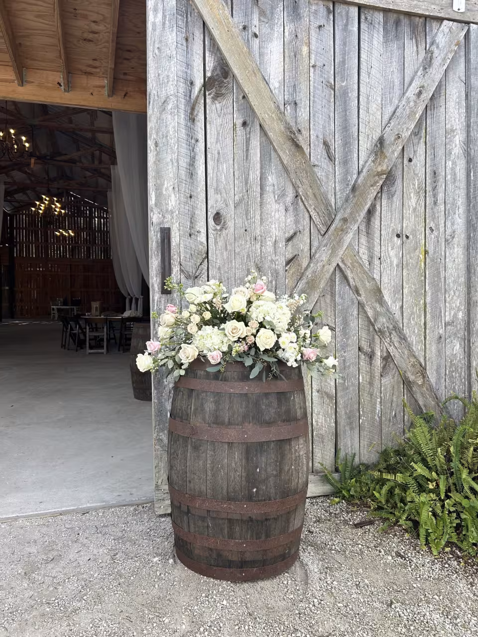 Barrel arrangement with white and blush roses at a rustic barn entrance