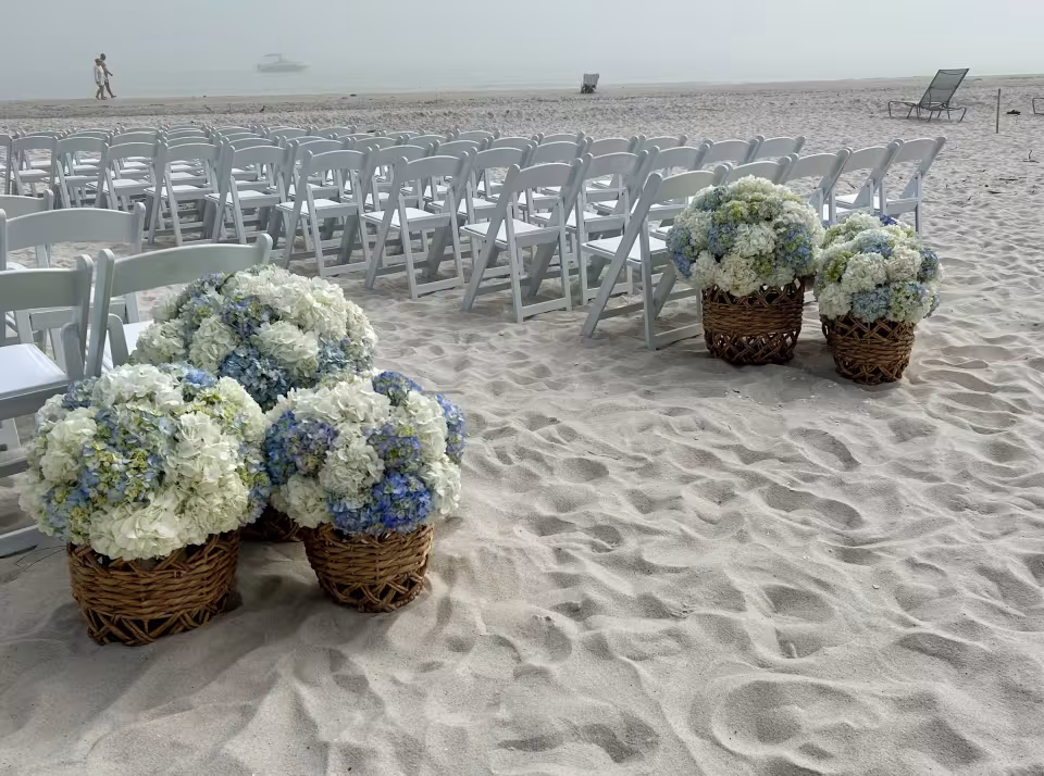 Blue and white hydrangea baskets on the beach beside ceremony seating